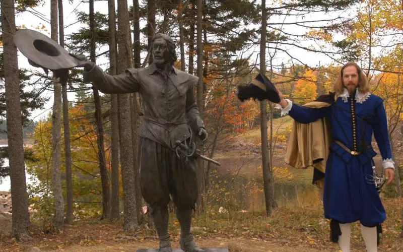 A bronze sculpture of Pierre Dugua with a reenactor standing nearby.