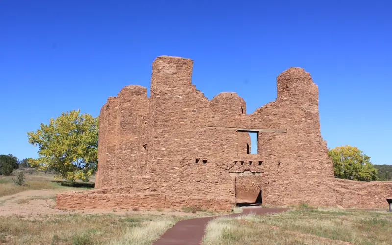 Stone walls of a roofless building rise into a bright blue sky.