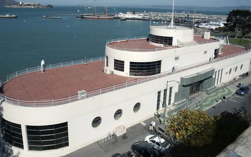 A red-roofed building with water and a pier behind it.