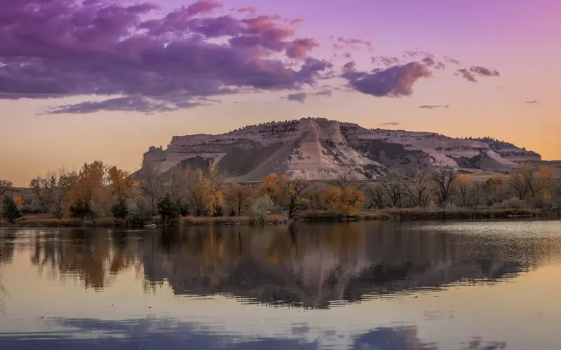 A pink sky and dramatic bluff are seen reflected in water.