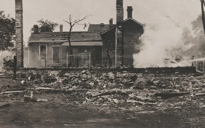 Historic photo of two people using a hose to extinguish a burning building.