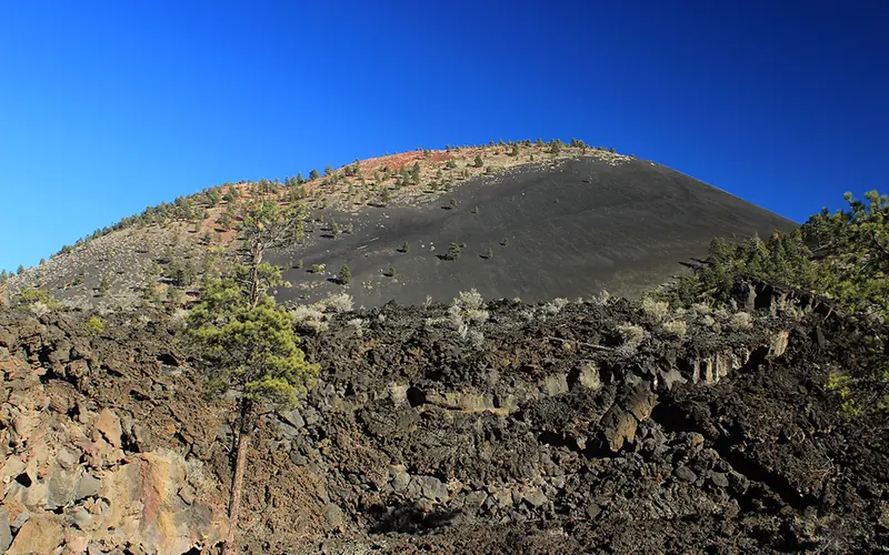 a jagged field of lava beneath a cinder cone volcano