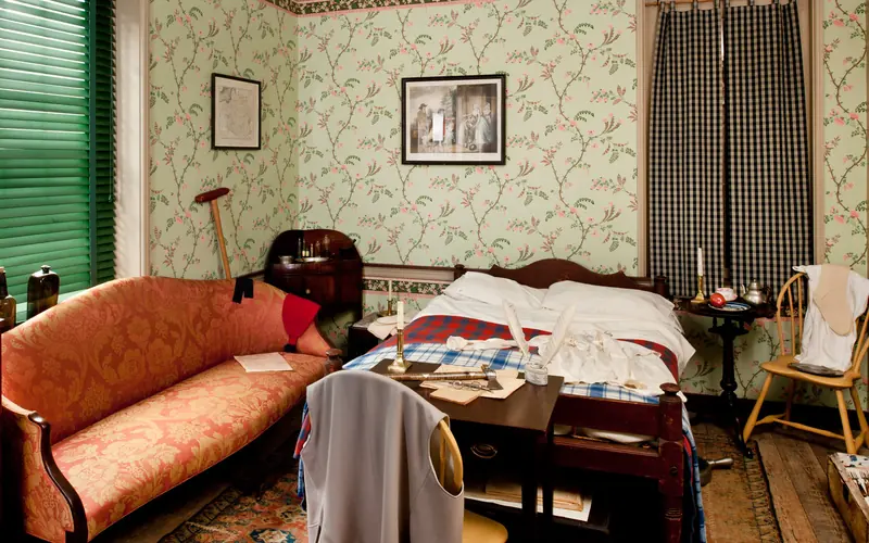 Color photo of the bedroom with a orange upholstered sofa and a bed in the small room.