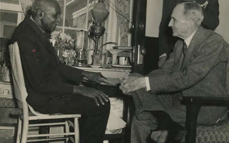 George W. Carver and Henry Ford seated facing one another talking