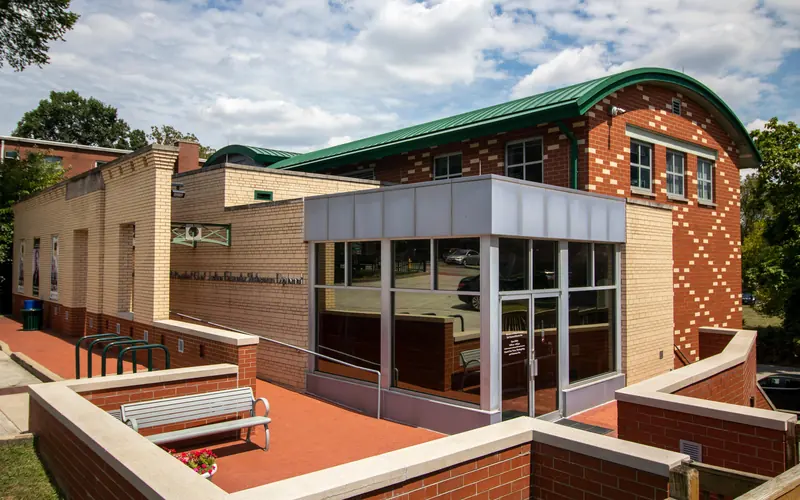 A tan and brick sided building with a corner entrance featuring tall glass windows and doors.