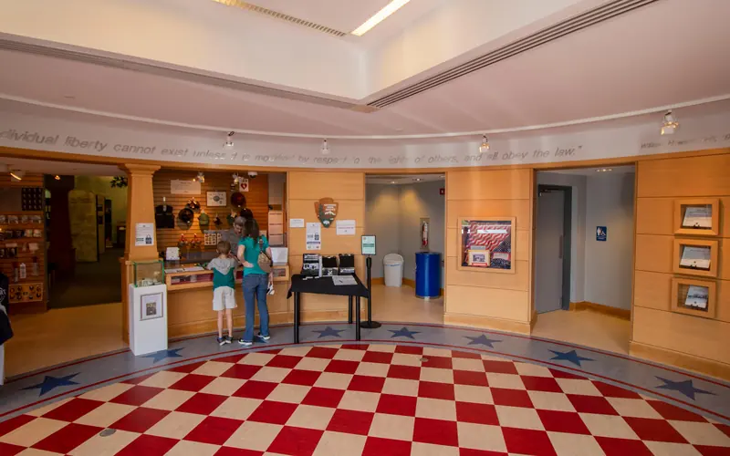 A lobby area with red and white square tiles and two people standing at a counter with a ranger.