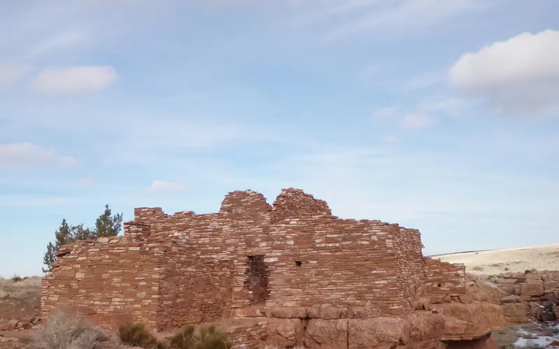 Walls of a white limestone and red sandstone structure under light blue skies with white clouds.